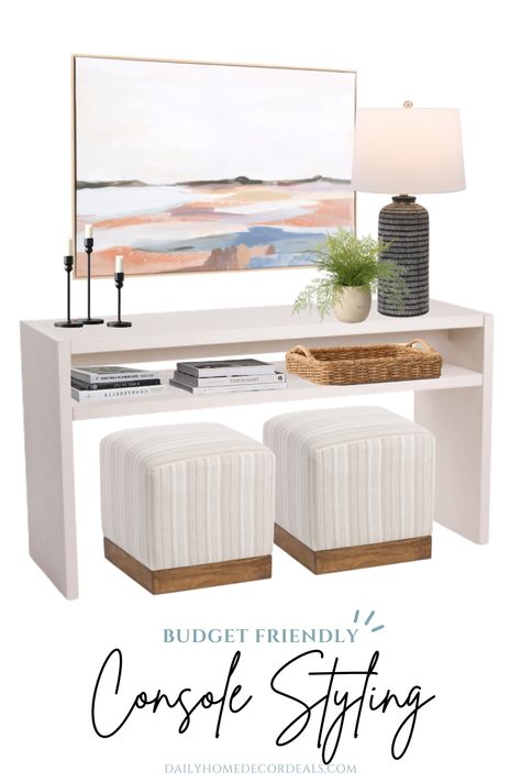 Affordable decor ideas for styling an open console table. Includes white wood console table with 2 square cube ottomans with beige and white striped pattern underneath. On the shelf is a woven wicker tray basket. On top of the console table is a black table lamp with a faux plant and 3 black metal candlesticks. Last, a budget-friendly framed watercolor artwork. The art is large oversized but very inexpensive featuring an abstract landscape of the seaside with blues, blushes, and gray tones. Console Table With Cubes Underneath, Console With Seating Underneath, Entry Console With Ottomans, Guest Bedroom Console Table, Ottoman Under Entry Table, Waterfall Console Table Styling, Console With Stools Underneath, Entry Table With Seating Under, Console Table With 2 Stools