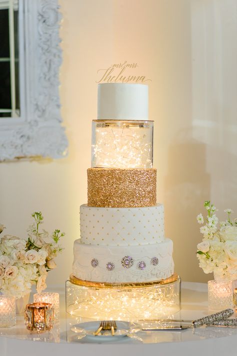 Elegant Bella Cosa Lakeside Wedding | white and gold wedding cake Gold And Cream Wedding Cake, Wedding Cake Fairy Lights, White Cake With Gold Accents, White And Gold Wedding Cake Elegant, Cakes With Lights, Cake With Fairy Lights, Glitter Cake Ideas, Cake White And Gold, Cake With Lights