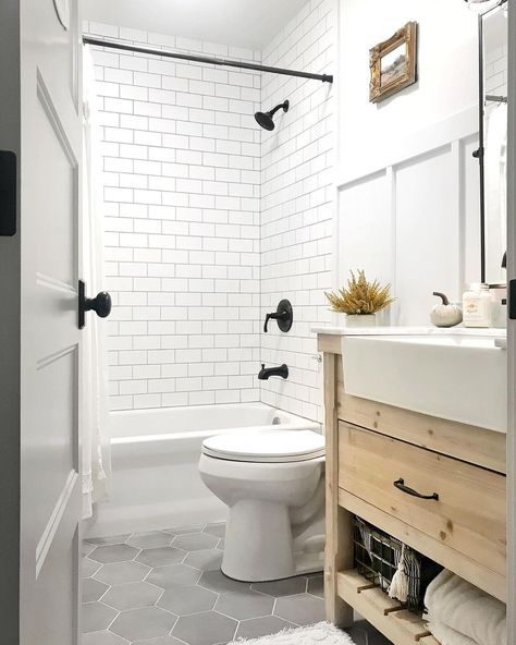 White tub and shower combo clad in white subway tile is fitted with a black faucet kit. A white toilet in front of the shower stands next to a light wood washstand in this gray hexagon floor tile bathroom. Hexagon Tile Bathroom Floor, Hexagon Tile Bathroom, White Subway Tile Shower, Grey Bathroom Floor, Tile Bathrooms, White Subway Tile Bathroom, Tile Tub Surround, Subway Tile Showers, Hexagon Tile Floor