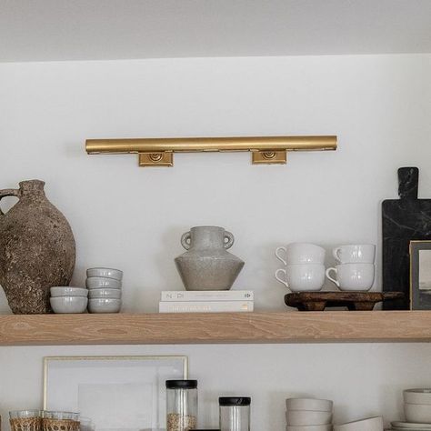 Visual Comfort & Co. on Instagram: "Shelfie appreciation post. 😍 Designer @rachaelbialkowski of @thelifestyledco⁣⁣⁣⁣⁠ helped her client @suzannavilla create a fresh yet timeless kitchen using a mix of neutral millwork and organic elements. Selected by the homeowner, the "cookies and cream" backsplash and countertop make a bold statement while pairing gorgeously with the white oak shelves for a natural look. Overhead, our iconic 30" Cabinet Maker's Picture Light by Chapman & Myers adds classic appeal to the space in a radiant Hand-Rubbed Antique Brass finish. The fixture brings a soft glow to the thoughtful collection of entertaining necessities and artful objects below. ​Architect: @harrisondesign 📷: @elizabethlaurengranger" Picture Light Kitchen Shelf, Gallery Kitchen Lighting Ideas, Picture Light In Kitchen, White Oak Shelves, Cream Backsplash, Kitchen Built Ins, Kitchen Bookshelf, Kitchen 2023, Bookshelf Lighting