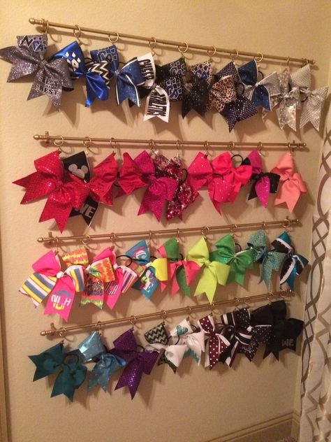 Cheer bow organization--I bought $3 curtain rods and clips with rings at Big Lots (spray painted gold) and attached the bows on the back loop (which doesn't damage the bow). After many years of figuring out how to organize these massive bows, I finally found a solution that works. She simply unclips the bow, wears it, and clips it back up! Cheer Bow Organizer, Cheer Bow Display Ideas, Cheer Bow Holder Diy, Cheer Bow Storage, Curtain Rods Diy, Bow Organization, Cheer Room, Nursery Organization Diy, Diy Bow Holder