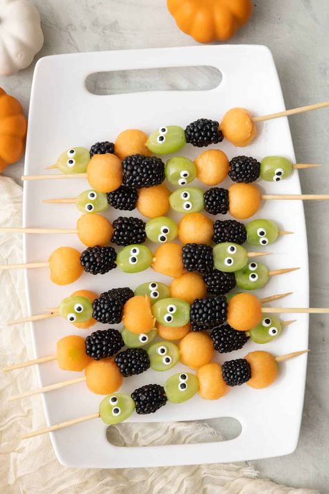 Get ready to spookify your taste buds with our Halloween Fruit Kabobs! These ghoulishly delightful skewers feature juicy cantaloupe balls that are like mini pumpkin orbs, grapes with mischievous googly eyes that seem to watch your every move, and plump, mysterious blackberries that add a dark twist to your fruit adventure. It's a fruity fiesta that's as playful as it is eerie – the perfect way to haunt your taste buds this Halloween! Grab one and take a bite, if you dare! | Halloween F Halloween Fruit Class Party, Thanksgiving Fruit Skewers, Fruit Kabobs Halloween, Pumpkin With Fruit Skewers, Spooky Fruit Salad, Halloween Fruit Skewers For Kids, Fruit Halloween Tray, Pumpkin Fruit Kabobs, Halloween Fruit Kabobs For Kids