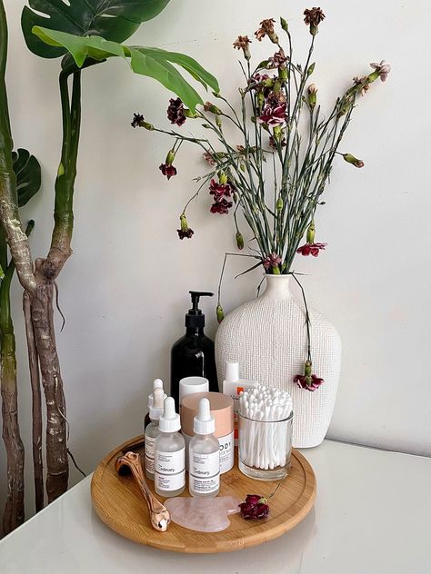 On a clean white desk there are magenta Flowers in a white vase, in-front of it is a wooden turntable with skincare products on it. Skin Care Desk Organization, Minimalist Skincare Organization, Skin Care Stand, Bathroom Skincare Display, Skin Care Display Ideas, Skincare Display Ideas, Flowers In Bathroom, Skincare Desk, Skincare Wall