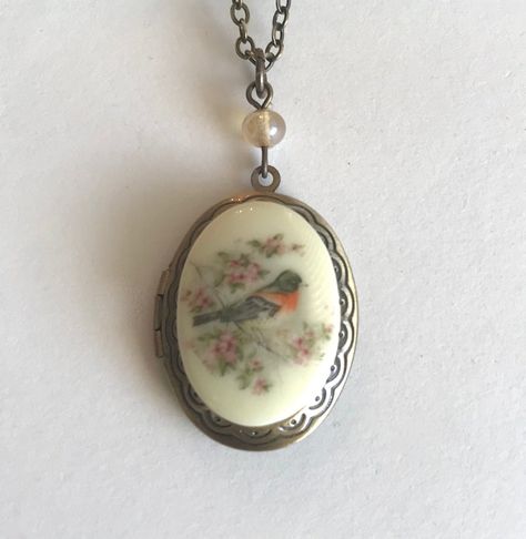 "Here is a pretty bird locket necklace. This necklace features an oval shaped brass locket with a vintage style cameo cabochon in the center. The cabochon depicts a sweet spring robin bird perched on a cherry blossom branch, the cameo is made from resin. This locket has an engraved floral pattern along the front side border and it is suspended from a glass bead. Locket comes on a sturdy soldered brass chain that is closed with a solid brass clasp. Perfect for spring or summer. All jewelry comes Unique Locket Necklace Silver, Vintage Necklace Antiques, Bird Locket, Robin Necklace, Locket Necklace Vintage, Side Border, American Robin, Victorian Locket, Blossom Branch