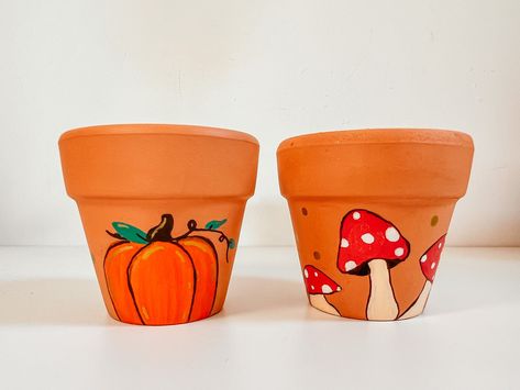 Add autumnal vibes to your home with these mini, ceramic clay terracotta pots that are perfect for your plant babies!  Each one has been carefully hand painted and is finished with a clear satin glaze to preserve the design. Dimensions: 6.6 x 4.1 x 6.4 Centimetres Halloween Painted Flower Pots, Mushroom Flower Pot, Halloween Pots Terra Cotta, Painted Pots Diy Terra Cotta, Mushroom Plant Pot, Halloween Pots, Mushroom Pumpkin, Painting Pots, Fall Pots