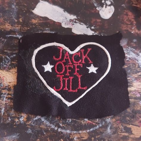 An unevenly cut, black, rectangle, fabric patch is on a paint-stained background. On the patch is a white heart, inside the heart, written in red, are the words "Jack Off Jill" in a vertical column. On either side of the word "Off" are white stars. Jack Off Jill Logo, Punk Shirts Diy, Diy Punk Pins, Punk Pins And Patches, Punk Patch Stencil, Punk Band Patches, Band Patches Diy, Jack Off Jill Band, Punk Patch Ideas