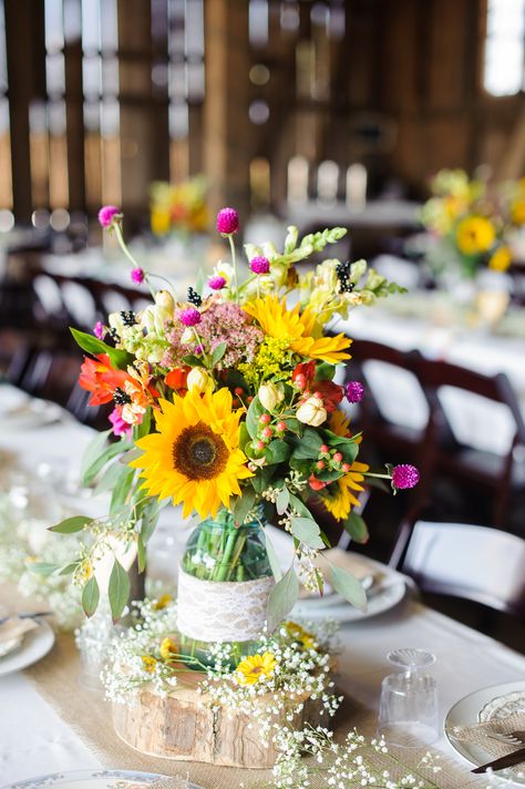 The mason jar centerpieces were filled with fuschia thistles, sunflowers, coral lilies, red hypercium and sedum. The mason jars were wrapped in burlap and lace and displayed on wood slabs. The burlap table runners were also decorated with baby's breath. Sunflower Wedding Centerpieces, Yellow Centerpieces, Wildflower Centerpieces, Sunflower Wedding Decorations, Wedding Centerpieces Mason Jars, Sunflower Centerpieces, Table Rose, Sunflower Themed Wedding, Country Chic Wedding