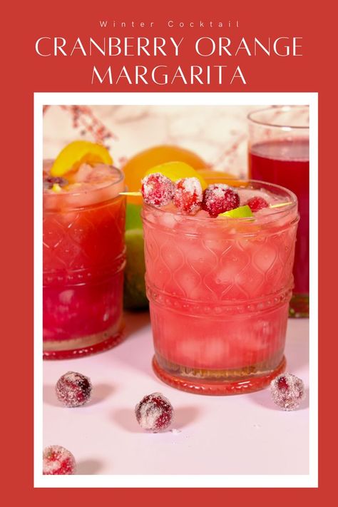 Glass filled with a cranberry orange margarita with sugared cranberries and lime slices as the garnish. Orange Cranberry Drink, Cranberry Orange Alcoholic Drinks, Cranberry Orange Juice Cocktail, Cranberry Jalapeno Margarita, Cranberry Margarita Recipe Pitcher, Cranberry Orange Spritzer, Holiday Margaritas Pitcher, Cranberry Orange Cocktail Drink Recipes, Cranberry Margarita Pitcher