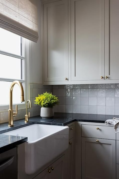 Kitchen features light gray cabinets with black marble countertop under gray glazed grid tiles and a farm sink with an antique brass gooseneck faucet. Dark Granite Countertops, Light Cabinets, Light Grey Kitchen Cabinets, Light Grey Kitchens, Light Kitchen Cabinets, Light Gray Cabinets, Black Granite Countertops, Black Countertops, Gray Cabinets