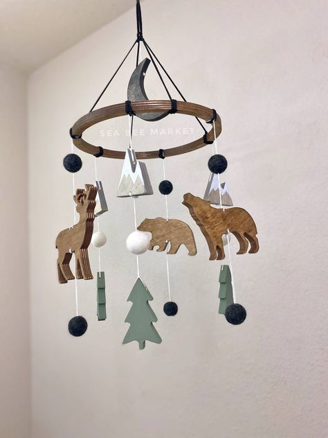 "This woodland crib mobile is one of my favorite designs. The mobile has everything to perfectly tie together your modern winter woodland, adventure, national park, or camping themed nursery.  The mobile comes complete with a few  snow capped mountains, one wolf, one bear, one buck/deer, three pine trees, a black moon, and charcoal grey wool balls. The colors perfectly contrast each other and are warm and inviting! The hanger is black faux leather/suede cord to tie together the perfect woodland Forest Green Crib Nursery, Adventure Nursery Ideas, Log Cabin Nursery Ideas, Black Bear Nursery Theme, Forest Baby Boy Nursery, Nursery Ideas Outdoor Theme, Wilderness Theme Nursery, Happy Camper Nursery, Alaska Themed Nursery