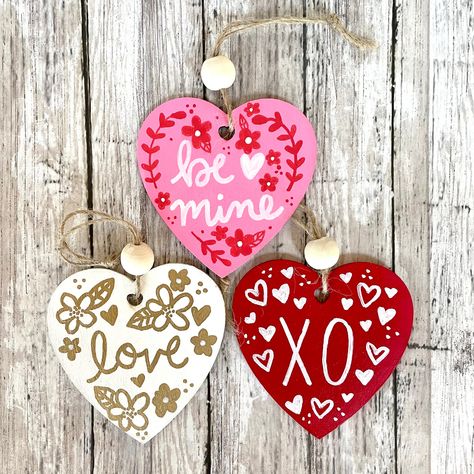 "This set of 3 hand painted heart Valentine's ornaments is the perfect gift or decor for Valentine's Day. Each set comes with 3 hearts adorned with \"Be Mine\", \"Love\" and \"XO\". The ornaments were painted using acrylic paint on wood ornament cutouts. Each ornament is adorned with a wood bead on the twine hanger. The ornaments you receive may vary slightly from the photo, as each one is individually painted and wood grain is unique. (100% hand painted, no stamping or vinyl) -3 inch wood heart Painted Valentine Hearts, Painted Wooden Hearts Ideas, Wood Heart Painting Ideas, Painted Wood Hearts, Wood Valentine Crafts, Painted Hearts On Wood, Wooden Heart Painting Ideas, Wooden Heart Crafts, Wood Heart Crafts