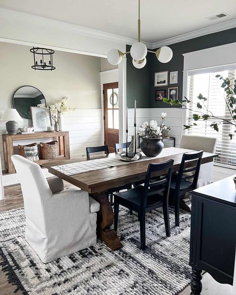 Shiplap half wall in entryway provides background for a wood console and black framed mirror. Shiplap wall continues into emerald green dining room with a modern chandelier over wood dining table. Varying black and white chairs sit around the table. Dining Room Entryway Combo, Shiplap Entryway, Dark Wood Table, Green Dining Room, Dark Green Walls, Front Door Entryway, White Shiplap Wall, Dining Ideas, Faux Brick Walls