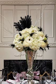 Black, white, and silver floral arrangement with feathers Gatsby Floral Centerpieces, Gatsby Floral Arrangements, 1920 Flower Arrangements, Great Gatsby Flower Arrangements, Gatsby Flower Arrangements, 1920s Flower Arrangements, Masquerade Ball Flower Arrangements, Art Deco Flower Arrangements, Masquerade Flowers