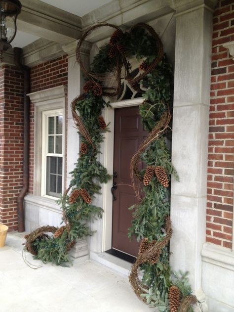 Christmas front door & entry decor - evergreen garland, grapevine, large pinecones, lights Grapevine Christmas Garland, Decorating With Grapevine Garland, Grapevine Garland Front Door Christmas, Grapevine Garland Front Door, Grapevine Garland Ideas, Front Porches Farmhouse, Outdoor Christmas Porch Decor, Evergreen Garland, Grapevine Garland