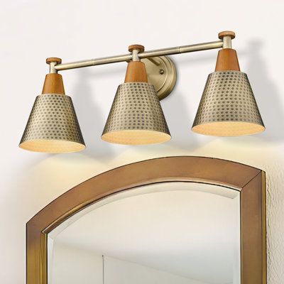 From the rustic wood grain finish to its minimalist design, this 3-light vanity fixture illuminates your bathroom with plenty of charming coastal style and lots of shine. It's crafted from steel, and it features a round, tapered backplate with exposed hardware. This vanity light includes three open, sconce-style fixtures with hammered cone-shaped shades crafted from metal that reflect the light down from 60W bulbs (sold separately). We love that this piece works well above the mirror in your ent Mid Century Modern Bathroom Vanity Light, Copper Light Fixture Bathroom, Boho Bathroom Lighting Over Mirror, Over Vanity Bathroom Lighting, Coastal Vanity Lighting, Barndo Lighting, Above Mirror Bathroom Lighting, Vanity Lighting Over Mirror, 3 Light Bathroom Vanity Light