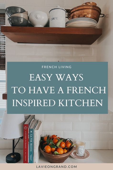 Kitchen counter with bowl of oranges, 3 French cookbooks and a candle. 2 dark wood shelves with plants and silverware. Small Parisian Apartment Kitchen, Small French Kitchen Ideas, French Minimalist Kitchen, Classic French Kitchen Design, Minimal French Decor, French Chic Kitchen, French Country Life, French Kitchen Style, Parisian Inspired Kitchen