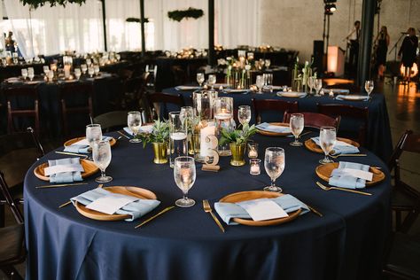 Navy Blue Wedding Reception Round Table Decor with Blue Satin Linen, Wooden Chargers with Dusty Blue Linen, Lasercut Table Number, Floating Candles in Glass Vases, Green Plant in Gold Vase | Lakeland Venue Haus 820 | Tampa Bay Rentals Over the Top Linens Wedding Reception Round Table Decor, Wedding Reception Table Linens, Succulent Wedding Centerpieces, Blue Wedding Receptions, Navy Blue And Gold Wedding, Round Table Decor, Blue Tablecloth, Wedding Table Linens, Wedding Reception Centerpieces