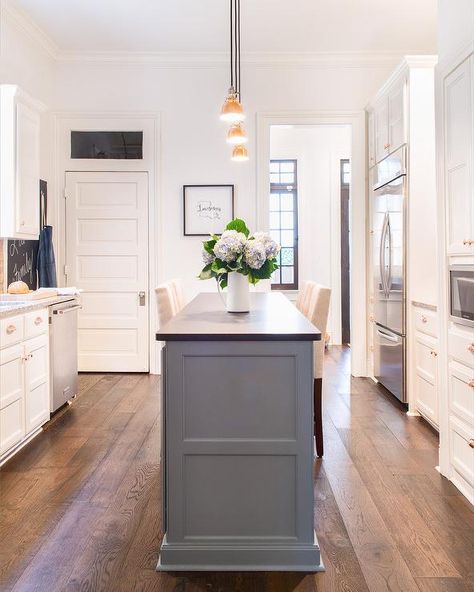 Cream upholstered counter stools flank a slim gray kitchen island topped with a black leathered granite countertop illuminated by three brass mini industrial pendants. Black Leathered Granite, Kitchen Island Granite, Gray Kitchen Island, Marble Top Kitchen Island, Upholstered Counter Stools, Leathered Granite, Kitchen Island With Granite Top, Best Kitchen Island, Narrow Kitchen Island