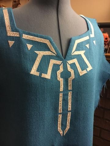 Malinda here again, and this past week I worked on Link's Champion tunic! I used applique for all the details, which is an easy technique to learn. I'll walk you through the process:   I drew my designs on paper first since I needed to duplicate them for symmetry. You can draw directly on the paper side of Heat n Bond or Wonder-Under (these can be found in the interfacing or notions section of your local fabric store), but make sure it's a mirrored version of the design. I... Champions Tunic Link, Link Tunic Pattern, Link Tears Of The Kingdom Costume, Link Champion Tunic, Botw Link Cosplay, Link Cosplay Breath Of The Wild, Link Costume Diy, Mipha Cosplay, Link Tunic