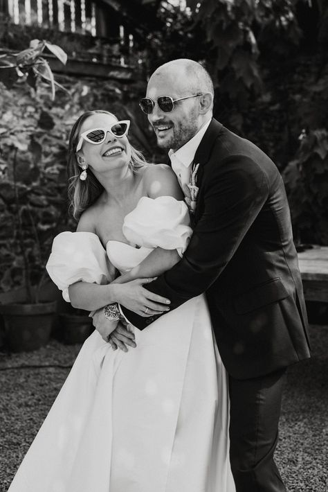 Groom wearing sunglasses hugs the bride from behind in a puff sleeve wedding dress with white sunglasses Bride White Sunglasses, Wedding Pictures With Glasses, Sunglasses With Wedding Dress, Bride And Groom Sunglasses Photo Ideas, Bride With Sunglasses Photo Ideas, Bridal Party With Sunglasses, Wedding Dress Sunglasses, Bride In Sunglasses, Engagement Shoot Sunglasses