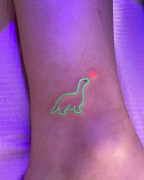 124 Glow-in-the-dark green dinosaur tattoo with an orange heart on foot under ultraviolet light. Trendy and unique body art. | Sky Rye Design Plur Tattoo Rave, Neon Tattoo Ideas, Uv Tattoo Ideas, Blacklight Tattoo, Glowing Tattoos, Purple Tattoo Ink, Glow In The Dark Tattoo, Uv Ink Tattoos, Invisible Art