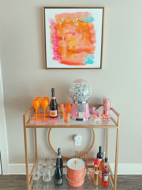 a cute gold bar cart with orange and pink accents. Decorative Bar Cart, Bar Cart Simple, Bright Bar Cart, Bar Cart Picture Frame, Good Bar Cart, Funky Bar Cart Decor, College Bar Cart Decor, Pink Bar Cart Aesthetic, Preppy Bar Cart Decor