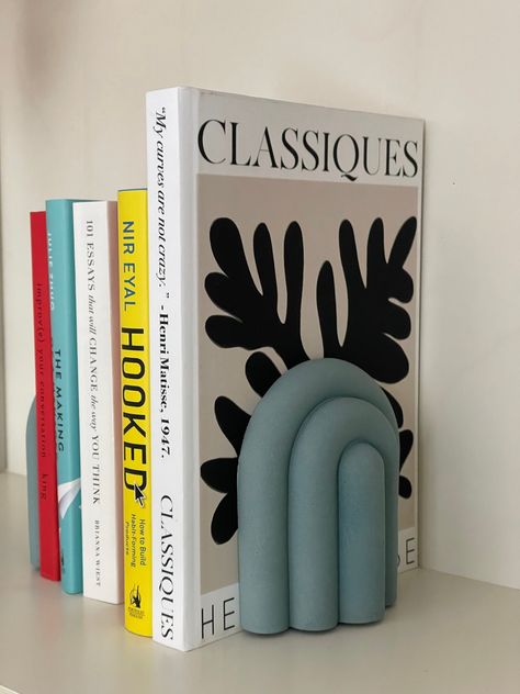 // FREE PICK UP in Toronto around Finch Station using code FREETORONTO at checkout // Elevate your bookshelf decor to a whole new level with our Nordic Elegance Bubbly Rainbow Bookend. This unique and eye-catching piece seamlessly blends minimalist design with a touch of whimsy, making it the perfect addition to your home or office. Crafted with precision and care, this bookend is a work of art that also serves a functional purpose, keeping your favourite books organized and stylishly displayed. All our products are handmade and made of natural raw concrete. Each piece may be slightly irregular and unique due to the nature of concrete, air bubbles and texture. Felt pads are applied to the bottom for scratch resistance. Comes in 2 pieces. Clay Bookends Diy, Diy Bookends Easy, Clay Book Ends, Pottery Book Ends, Air Dry Clay Bookends, Book Ends Aesthetic, Bubble Ceramics, Clay Bookends, Pottery Bookends