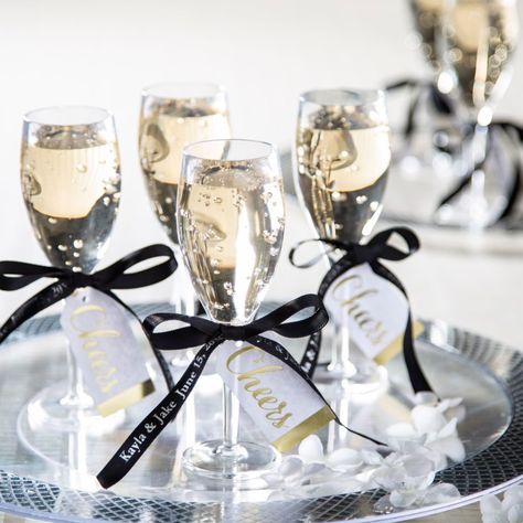 Wrapped in a black ribbon carrying your unique message, these chic shot glasses bring a toast to unforgettable moments with each sip. Perfect for adding that dash of sparkle to wedding receptions, bridal showers or rehearsal dinners, these timeless keepsakes make your celebration a bubbly joy to remember! (31 pcs. per unit)Includes:o 1 Satin Personalized Black Ribbon (The message of your choosing will repeat approximately every 4" for the entire 25 feet of satin ribbon. Personalize with 1 line of up to 32 characters/spaces. 3/8" x 25 ft.)o 6 Plastic Champagne Shot Glasses (1 3/4" 2.5 oz.)o 24 Cardstock Cheers Gold & White Favor Tags (2 1/2" x 1 1/4")o Assortments are subject to change at any time and may vary from picture shown. Substituted items will be similar in nature. Fancy Champagne Aesthetic, Bridal Shower Drink Table, Bridal Shower Chic, Champagne Glasses With Ribbon, Black Bridal Shower Theme, Bridal Shower Ideas Black And White, Bridal Shower Black And White, Bridal Shower Glasses, Chic Engagement Party