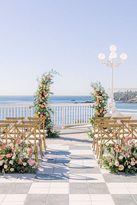 This is a micro/ small/ intimate wedding ceremony setup that has a stunning view overlooking the water and cliffs of the Southern California beach. This beautiful venue is Occasions at Laguna Village in Laguna Beach, CA. This set up is complete with X-back chairs, flower ceremony arch, and other ceremony florals. The main colors for this citrus wedding are shades of pink with a lot of greenery. Beach Terrace Wedding Ceremony, Beach Backdrop Wedding, Citrus Wedding Ceremony, Small Wedding Ceremony Chair Setup, Beach View Wedding Ceremony, Summer Wedding Venues Outdoor Ceremony, Lake View Wedding Ceremony, Wedding Overlooking Water, Pastel Arch Wedding