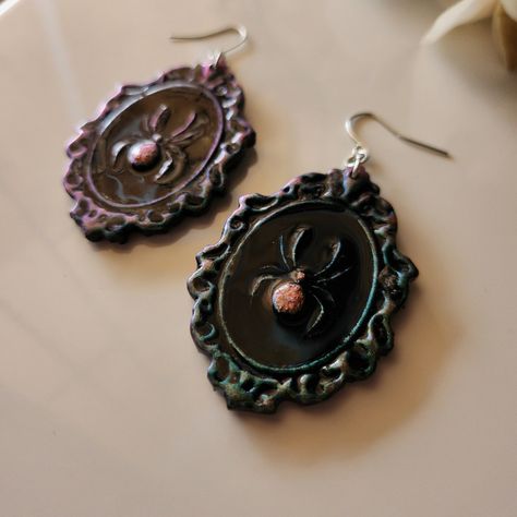 Handmade Polymer clay earrings Spiders in a Victorian frame. These duo-chrome earrings are beautiful in the sun! They shift between a teal-blue color and a maroon-brown shade.  *Hypoallergenic  *Lightweight *Handmade and unique Care Instructions: Clean metal parts with rubbing alcohol before use. Avoid contact with water, oils and perfumes. Store in a clean and dry area. Gently clean with a soft damp towel if needed. Polymer clay earrings are durable but be careful not to bend or drop earrings as they may break.  Each pair of earrings are handmade, unique and made to order. Slight variations may occur in shape, color and texture. My pieces have imperfections and differences but that to me is what makes them beautifully unique! I primarily use polymer clay to create my jewelry but other med Gothic Clay Jewelry, Goth Clay Earrings, Goth Polymer Clay, Chrome Earrings, Jewelry Alternative, Clean Metal, Victorian Frame, Diy Earrings Polymer Clay, Goth Earrings