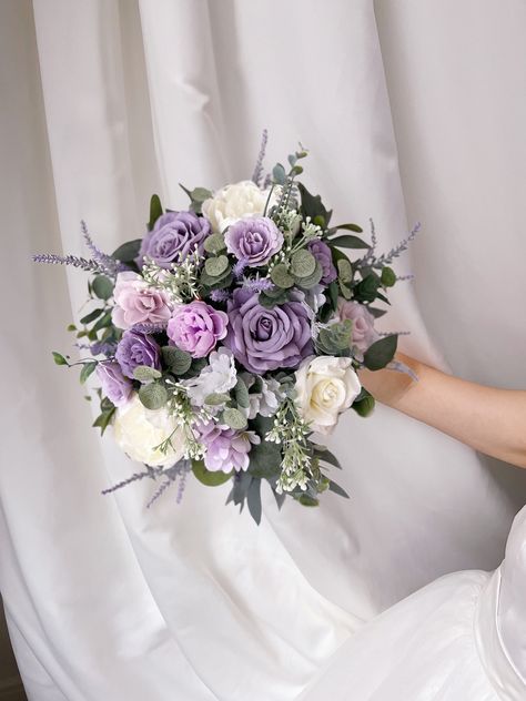 "More beautiful wedding flowers https://bridalstoryus.etsy.com  Lavender bridal wedding bouquet is created with high quality silk flowers. These handmade artificial wedding bouquets make beautiful additions to wedding and event floral arrangements. Flowers: lavender, peonies, roses, eucalyptus and fillers.  Colors: lavender, lilac, white, pale champagne, green. Handle: wrapped in ivory satin ribbon. Size: bridal bouquet is approximately 14\" wide, bridesmaids bouquet is 8\". SUGGESTION: steaming the bouquets, boutonnieres, corsages upon receiving them and you will see how easily they will take the original shape and wrinkles will be removed too. Purchase options:  PRICES ARE FOR THE 1 ITEM ONLY! * Bridal bouquet 14\" * Bridesmaids bouquet 8\" * Boutonniere * Corsage * Boutonniere #1 is wra Lavender And Lilac Bridal Bouquet, Lilac Flower Bouquet Wedding, Flower Bouquet Purple And White, Lilac And Eucalyptus Bouquet, Sage Green And Lavender Bouquet, Lavender And Sage Wedding Bouquet, Lilac Decor Wedding, Purple Cascade Bouquet, Lilac Bride Bouquet