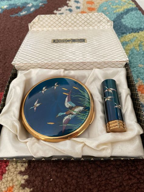 Vintage Kigu England compact set. Beautiful iridescent enameled flying mallard and cattail design. The powder compact has puff intact and lipstick case has direction insert. Both in unused condition.The detail is amazing and this will make a gift to be treasured.