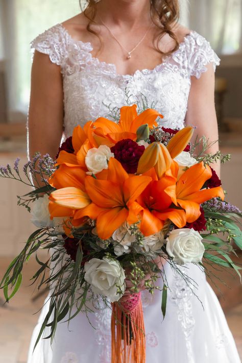 This unique bride has a custom bouquet with orange lilies, white roses, and lavender and green accents. You can recreate this with Asiatic lilies, either Brunello lilies or fire king lilies. This orange asiatic lily bouquet also has a macrame wrap dyed to match. Photo by Nallayer Studios. Tiger Lily And Rose Bouquet, Orange Lily Wedding Bouquet, Asiatic Lily Bouquet, Fire Bouquet, Tiger Lily Wedding Bouquet, Lilly Bouquet Wedding, Tiger Lily Bouquet, Rose And Lily Bouquet, Tiger Lily Wedding