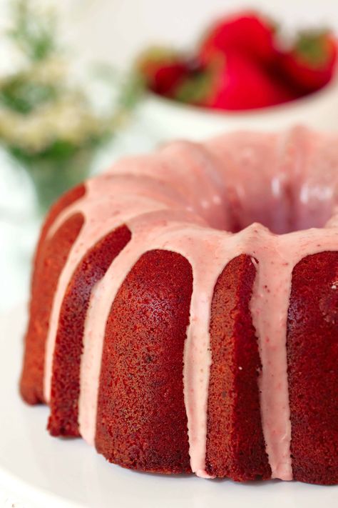 A side view of a whole Strawberry Pound Cake sitting on a white cake plate. It has been drizzled with a pink glaze and there are fresh strawberries and flowers in the background. Moist Strawberry Bundt Cake, Strawberry Cake Recipes Homemade, Homemade Strawberry Cake From Scratch, Strawberry Crunch Pound Cake, Pound Cake Icing, Strawberry Glaze Recipe, Strawberry Bundt Cake, Cakes Strawberry, Strawberries And Flowers