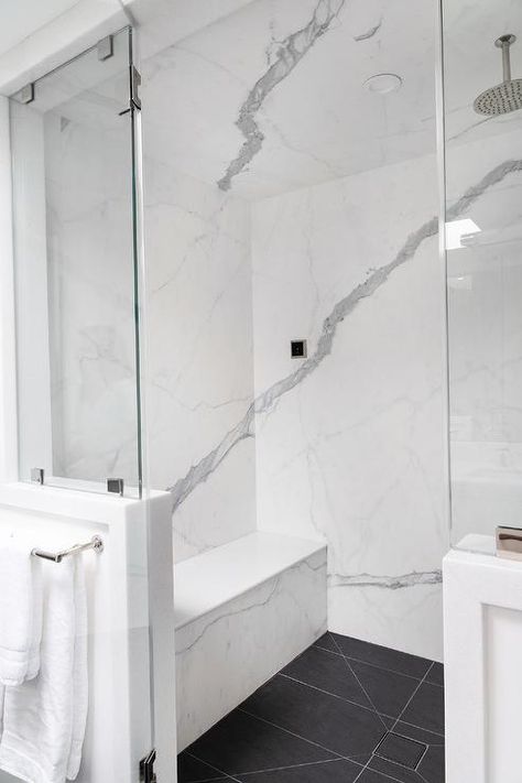 A round rain shower head is fixed to white and gray marble shower ceiling over black floor tiles ending at a marble bench fixed against a marble surround. Shower Ceiling, White Marble Shower, Marble Bench, Black Marble Tile, Marble Shower Tile, White Marble Bathrooms, Black Floor Tiles, White Marble Floor, Marble Showers