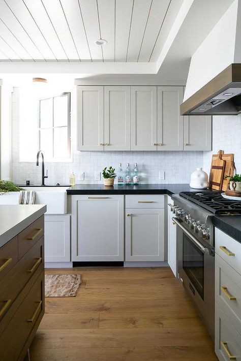 Light gray cabinets in a cottage kitchen feature black quartz countertops, white glazed backsplash tiles, and brass hardware. White Shaker Style Kitchen, Kitchen Black Counter, Light Grey Kitchen Cabinets, Greige Kitchen, Black Kitchen Countertops, Light Grey Kitchens, Light Gray Cabinets, Black Countertops, Grey Countertops