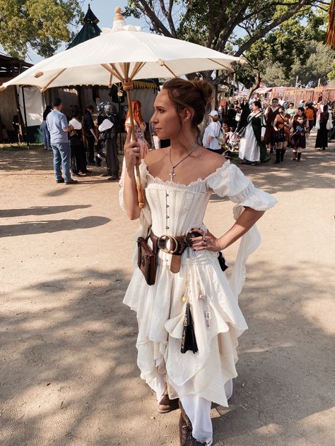 White woman with blonde hair tied into a bun, wearing a white gown with white corset. A leather belt carrying a book and chatelaine. She’s holding a white parasols. Ren Fest Costumes Women Shoes, Medival Outfits Woman Pants, White Ren Faire Outfit, Rem Faire Costume, Rennassaince Faire Outfits, Ren Faire Wench, Rennaisance Faire Outfit Fairy, Renn Faire Costume Women, Reinessance Fair Outfit