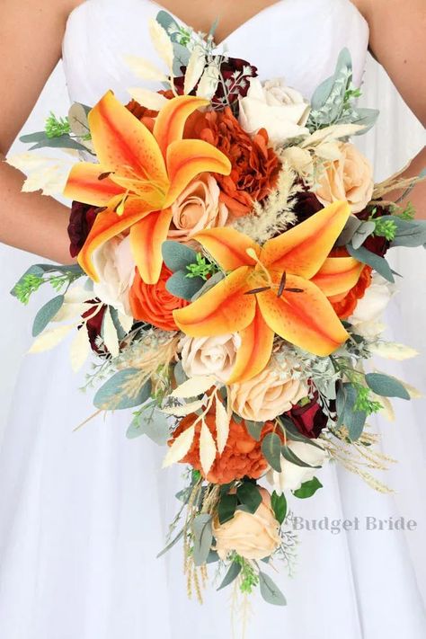 This is a cascading brides bouquet with burnt orange, apricot and champagne roses accented with orange lilies, mixed greenery and pampas grass. All of our wedding bouquets are made with artificial wedding flowers. Tiger Lily Bouquet Wedding Fall, Fall Floral Wedding Bouquets, Fall Wedding Bouquets Lilies, Bride Bouquets Tropical, Tiger Lily Wedding Cake, Tiger Lily And Rose Bouquet, Flowers For Orange Prom Dress, Champagne And Orange Wedding, Tiger Lily Wedding Decor