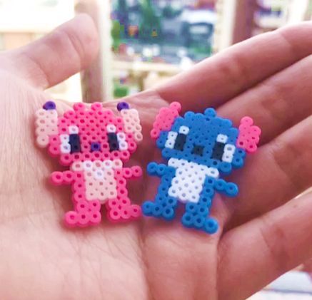 Uma mão cor de pele clara aberta, segurando dois bonecos, um da Angel(rosa e rosa claro) e um do Stitch(azul e branco) do filme Lilo & Stitch, feito de hama beads ou perler beads, que são como bolinhas, para fazer artesanato, formas, personagens, etc. Perler Beads Stitch, Hama Beads Disney, Hama Disney, Beads Stitch, Mini Hama Beads, Angel Stitch, Melty Bead Designs, Beads Perler, Modele Pixel Art