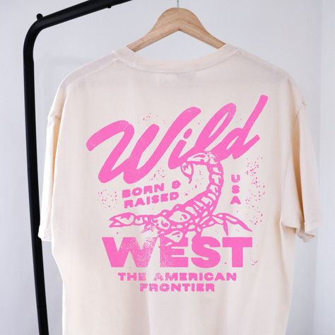 🤠Embrace the spirit of the Wild West with our "Wild West Born & Raised" graphic tee! This vintage-inspired shirt features a bold pink design that pays homage to the rugged American frontier. Perfect for your country concert or your night out in Nashville! 🔥 Stand Out in Style: Whether you're hitting the rodeo or just hanging out with friends, this graphic tee is sure to turn heads and start conversations. Pair it with your favorite jeans or shorts for a casual yet cool look that's perfect for any occasion.  🖤SHIRT MATERIAL Comfort Colors Unisex Shirt 100% Ring-Spun Cotton Printed using Direct To Garment style- Inks are printed directly into the fabric. Different sizing may effect placement of final design. Colors may differ slightly due to different user monitor and screen settings.  🏁 Female Graphic Tees, Country Concert Tshirts, Pink T-shirts, Concert T Shirt Design, Trendy Oversized T Shirts, Fun Shirt Designs, Wild West Design, Punk Tshirt Design, Tour Tshirt Design