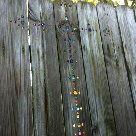 I had seen the random marble placement of marbles in a fence and decided to create a cross. My awesome husband went to craft store with me where we found no marbles and decided to go with glass beads. We cut a couple of bead strands that were made for necklaces and bought a box of mixed beads. Awesome husband continued awesomeness by drilling all the holes for me after we drew a cross with a level for only a simple outline. The rest was freehand.  Try it! It's fun and when the light gets behind Marble In Fence, Marbles In Fence Holes, Fence With Marbles In It, Marbled Fence, Marbles In Fence, Marble Fence, Awesome Husband, Front Yard Fence, Bamboo Garden