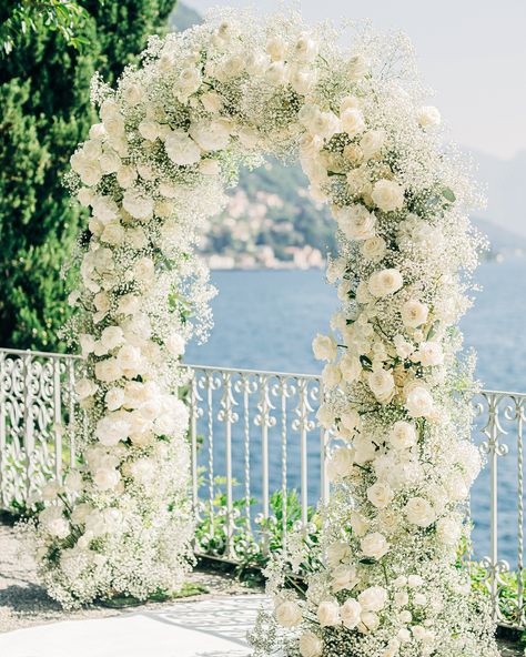 The majestic all-white wedding arch blends seamlessly with this stunning location! White gypsophila, roses and hydrangeas All White Arch Wedding, All White Flower Arch, White Rose Ceremony Arch, Outdoor Wedding Entrance Decor, Small Outdoor Ceremony, White Flower Arch Wedding Outdoor, White Hydrangea Wedding Arch, White Roses And Babies Breath Wedding, White Flowers Wedding Ceremony