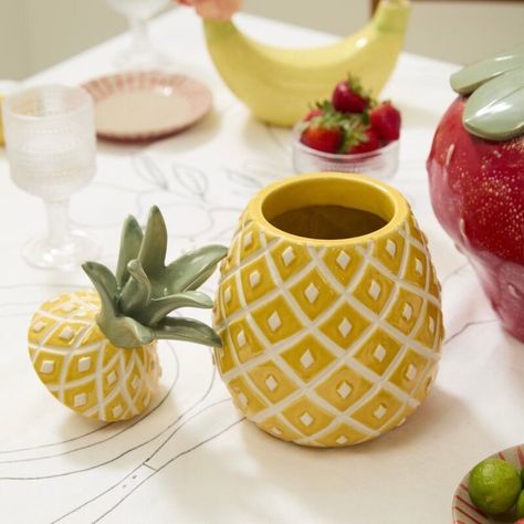 Experience the fun and fruity vibes of the Pineapple Canister! This food-safe ceramic cookie jar is adorned with vibrant hand-painted details and a yellow reactive glaze, giving it a unique and playful touch. Complete with a removable stem lid and dimensional seeds, this quirky and trendy piece is the perfect addition to your kitchen decor. Pair it with our other fruit-inspired tableware for a coordinated and summery everyday or event look. 6.5"Wx12"H Fruit Themed Kitchen, Pineapple Vase, Ceramic Pineapple, Fruit Decor, Ceramic Cookie Jar, Pineapple Decor, Reactive Glaze, Candle Tray, Kitchen Themes