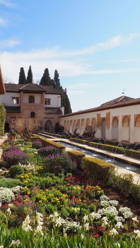 A photo of the flower garden at the Alhambra palace in Granada, Spain. The skies are blue and the flowers are multiple colors that line a fountain down the middle of the garden. Alhambra Palace Garden, Spain Alhambra Palace, Granada Alhambra Palaces, Granada Spain Aesthetic, Alhambra Garden, Islamic Gardens, Spanish Palace, Spanish Landscape, Spanish Flowers