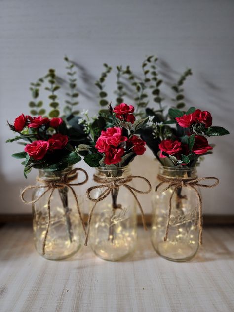 "These beautiful faux mini-rose quart size mason jar centerpieces are a Glassy Gal original design. Each centerpiece includes one set of warm white LED fairy lights, a jute bow, a deluxe faux greenery arrangement with mini roses. You can choose your mini rose color at checkout. These centerpieces are very popular for weddings, baby showers, parties, corporate events, holiday events, and any other event that requires table centerpieces. They also look great in any room of your house or office. To see other lighted jar options and all of my other listings, please view my shop: https://www.etsy.com/shop/GlassyGalDecor Each jar set includes: (1) clear quart size mason jar (1) set of LED fairy lights (1) deluxe faux greenery arrangement (includes 3 tall eucalyptus stems, 2 short silver dollar Table Decoration With Lights, Restaurant Centerpieces Simple, Small Elegant Centerpieces, Rose Themed Birthday Party Decorations, Black And Red Centerpieces, Valentine Table Centerpieces, Red And Gold Centerpieces, Valentines Table Centerpieces, Valentines Centerpiece Ideas