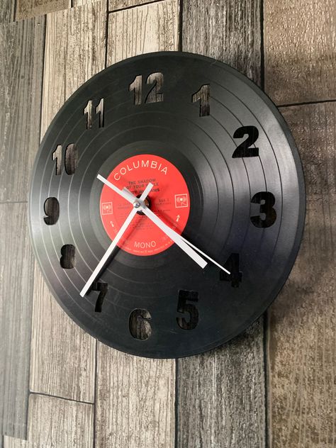 Make a statement to your space with this Vintage Vinyl Record Wall Clock. Made out of recycled records, this clock not only looks good but is eco-friendly as well! Each clock is made from a unique vinyl record that has been recycled so every clock is different! Made with a high quality quartz mechanism and retro style  hands allows it to keep time efficiently and accurately. Hang up the included album cover for an added touch.  Color of record varies. Cover for record varies. Measures 12" in dia Retro Style Room Decor, Wall Clock Aesthetic, Diy Clock Ideas, Funky Clock, Recycled Records, Vinyl Record Wall Decor, Vinyl Record Projects, Clock On Wall, Clocks Aesthetic