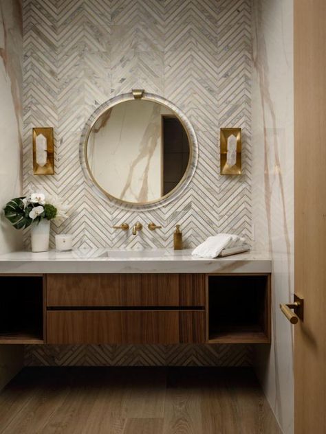 Mosaic tile laid in a fun zigzag pattern makes this backsplash the focal point in this contemporary bathroom. The neutral space has marble walls, hardwood flooring and a warm wood floating vanity. Gold accents, including sconces and faucet hardware, are the luxe finishing touch. Texas Lake House, Tufted Ottoman Coffee Table, Faucet Hardware, Star Pendant Lighting, Ceiling Shelves, Mosaic Tile Backsplash, Mosaic Bathroom, Island Countertops, Hall Bathroom