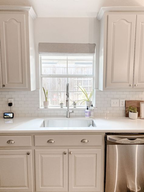 Neutral kitchen with gray cabinets, nickel accents and marble backsplash. Roman shade over kitchen window. Small Kitchen Window Over Sink, Make Your Kitchen Look Bigger, Kitchen Blinds Above Sink, Light Above Kitchen Sink, Decorating Above Kitchen Cabinets Ideas, Small Kitchen Window, Over Kitchen Sink, Above Kitchen Sink, Kitchen Sink Lighting