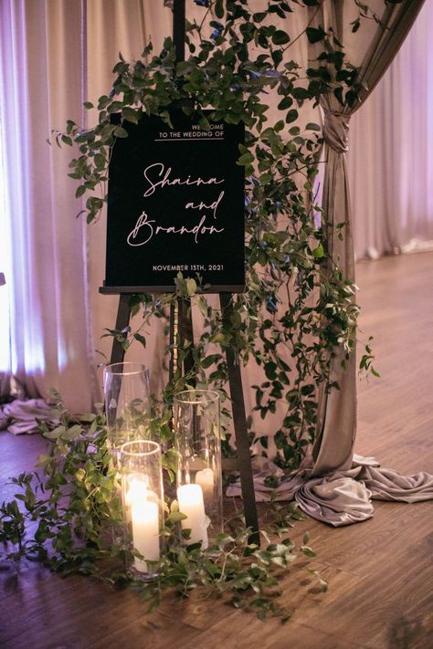 Wedding welcome sign with greenery vines and hurricane candles Wedding Vines Decor, Greenery Garden Wedding, Green Vines Wedding Decor, Vine Wedding Decorations, Wedding Welcome Sign With Candles On Floor, English Ivy Wedding Decor, Wedding Welcome Sign With Greenery, Welcome Sign Wedding Greenery, Flower Display Wedding