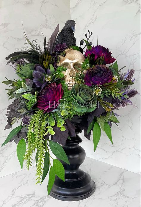 Polyresin, stone powder, and iron Skull with a Crow nestled on a Black Wood Pillar Candle Holder adorned with Handcrafted and hand painted Wood Flowers 3” in size in Dark Green and Purple shades with a hint of sparkle, the arrangement is accented with Faux Berries , Succulents & Greenery, Preserved Reindeer Moss in Forest, Black Maple Leaf Coiled Garland, Feather accent! Measures Approx.: 17”T x 12”W x 11.5” D *For Indoor Use Only Halloween Flowers For Grave, Moss Wreath Halloween, Halloween Silk Flower Arrangements, Fall Candle Wreath Centerpiece, Halloween Flower Centerpieces, Halloween Floral Design, Halloween Flower Arrangements Florists, Halloween Bouquet Decoration, Green And Black Halloween Decor